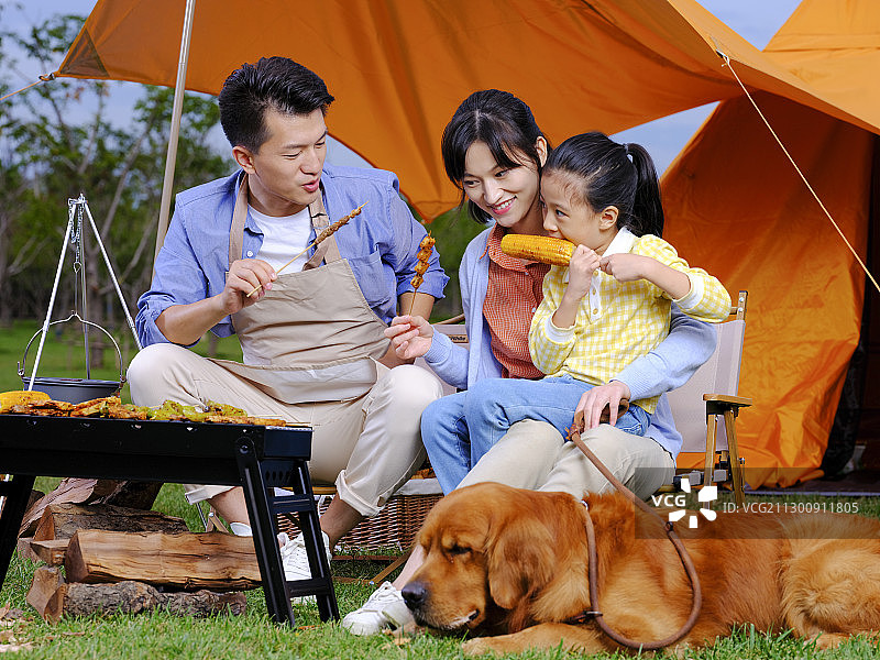 快乐的三口之家和宠物狗在公园烧烤图片素材