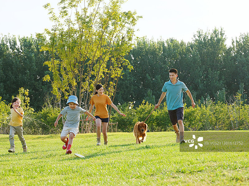快乐的四口之家和宠物狗在公园玩耍图片素材
