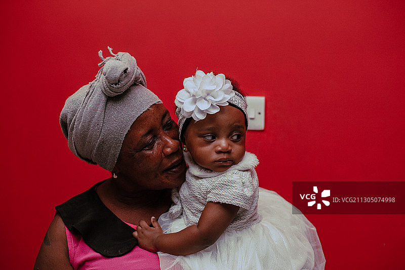 黑祖母抱着孙女靠在红墙上图片素材