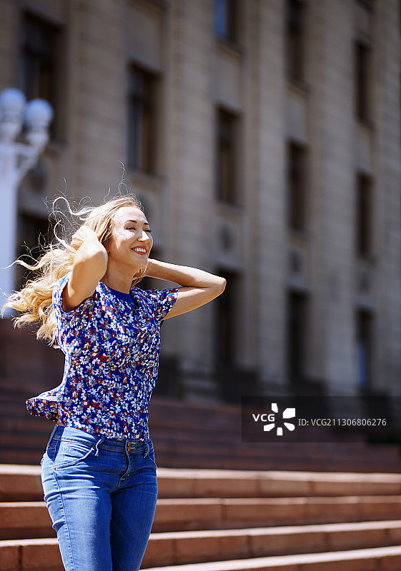 头发被风吹起的快乐女人在城市里享受阳光图片素材