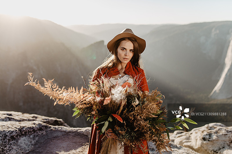 肖像美丽的女人戴着帽子，手持鲜花，而站在悬崖俯瞰山谷图片素材