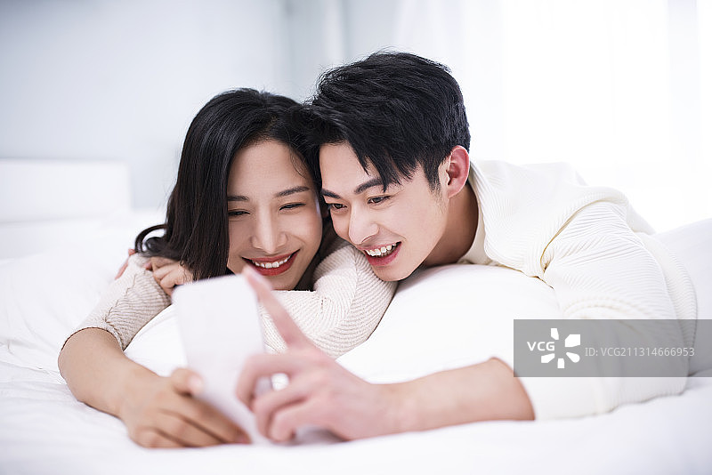 年轻夫妇躺在床上使用智能手机自拍图片素材