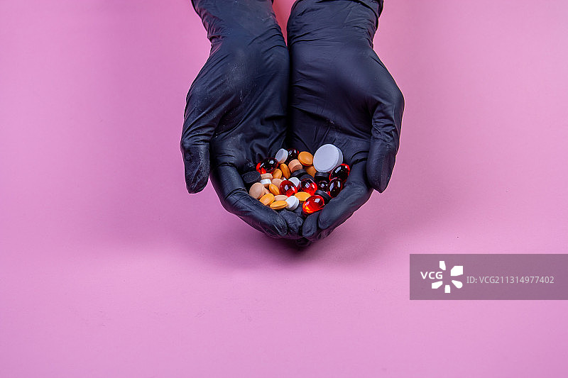 戴着手套的人的手拿着各种药丸和药物在粉红色的背景图片素材