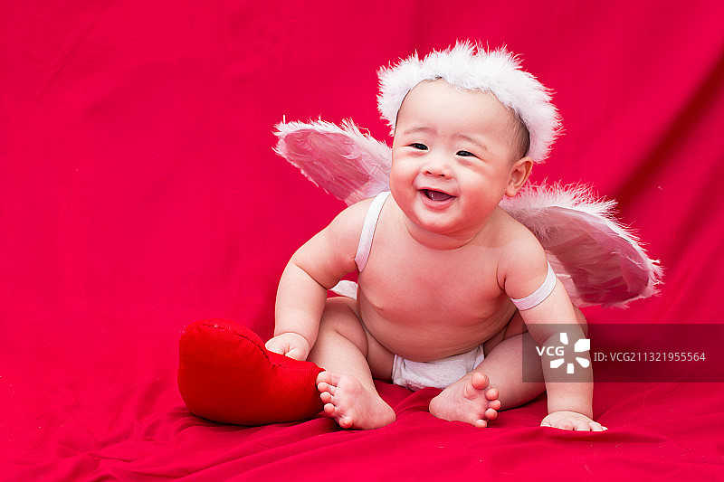 可爱的婴儿在天使服装坐在红色纺织品图片素材
