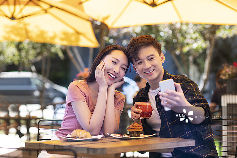 年轻情侣在户外咖啡厅用手机自拍图片素材