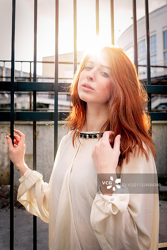 美丽的年轻红发女人站在黑篱笆前日落，都灵，意大利图片素材