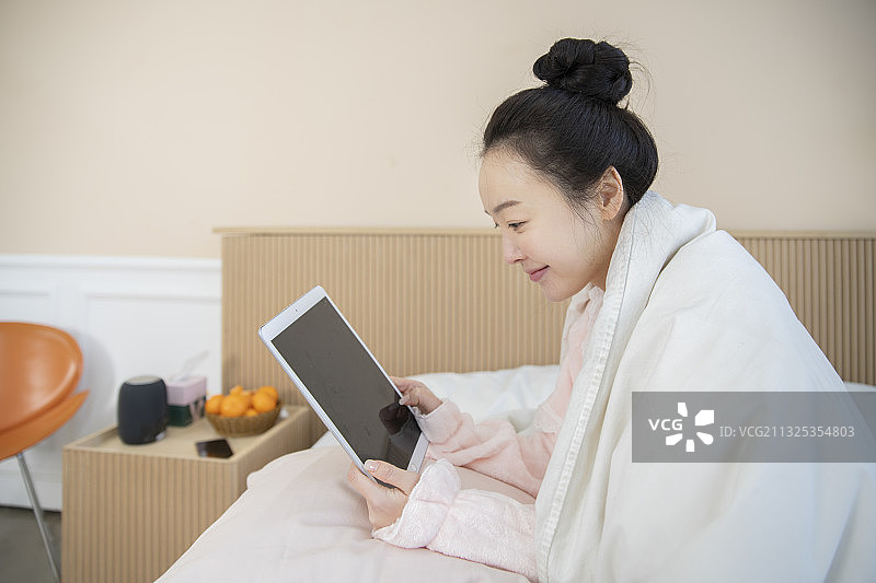 亚洲女人穿着睡衣在毯子下使用数码平板电脑图片素材