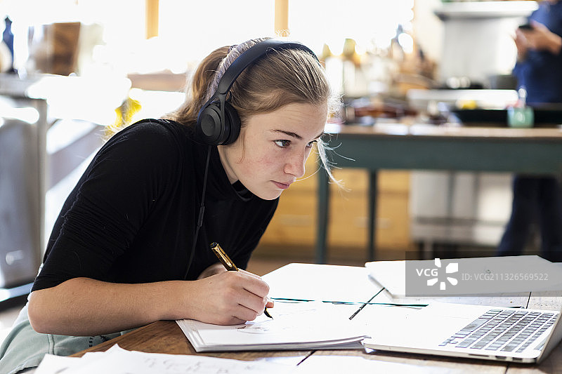 家，美国，十几岁的女孩戴着耳机，在纸上画画图片素材