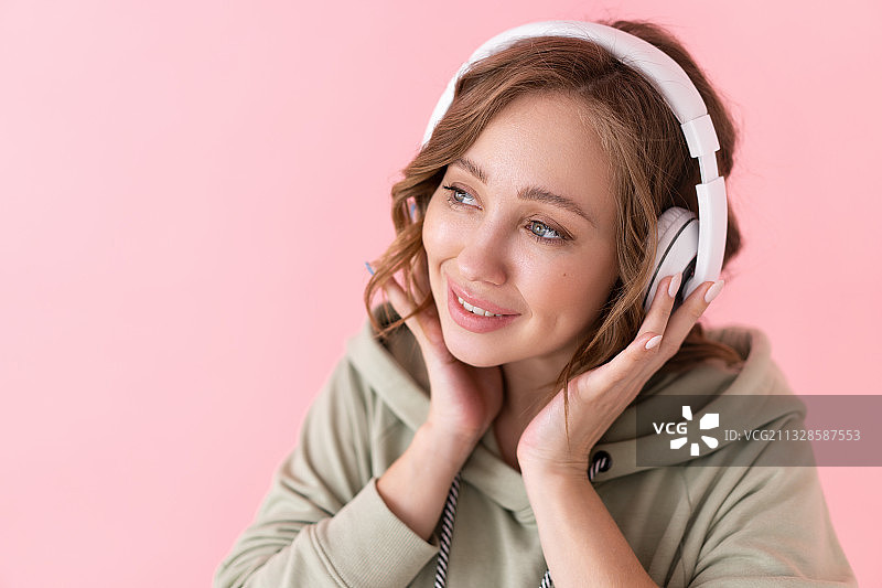 微笑的年轻女子戴着耳机，粉红色的背景图片素材
