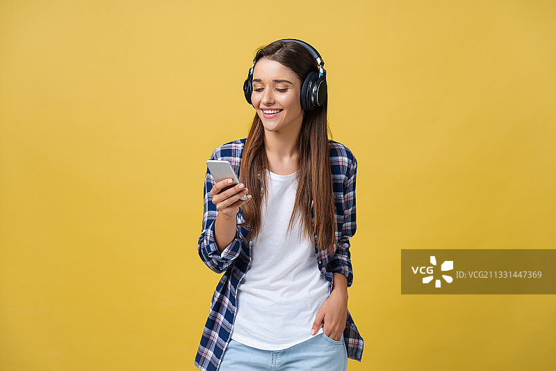 微笑的年轻女子听着音乐，站在黄色的背景下图片素材