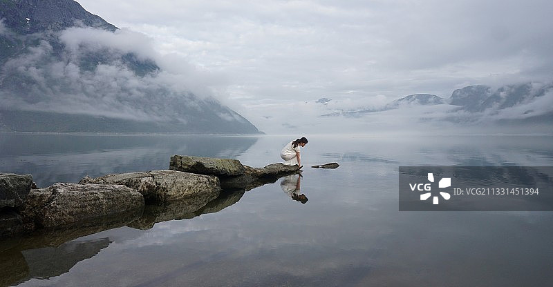 坐在挪威哈当厄峡湾湖边的一块岩石上的女人图片素材
