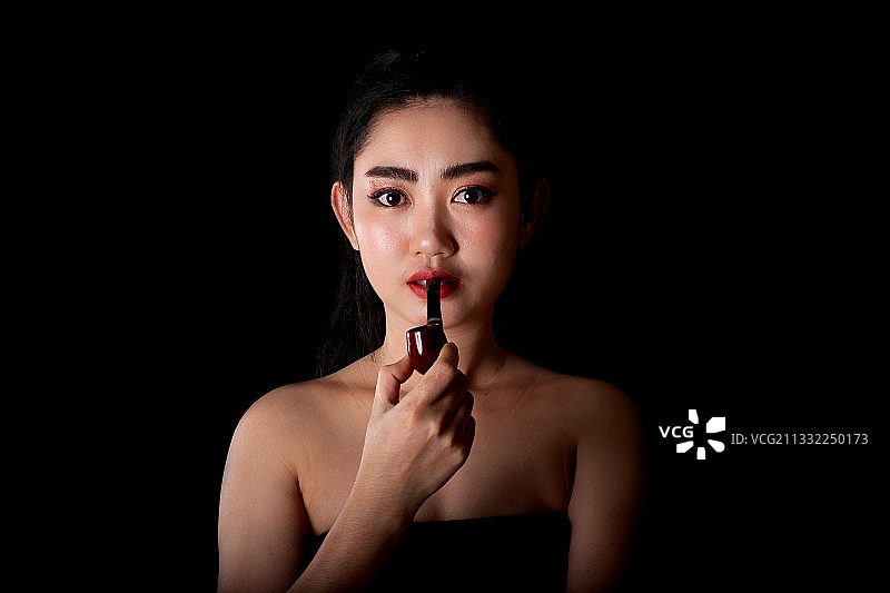 泰国，年轻女子在黑色背景下涂口红的肖像图片素材