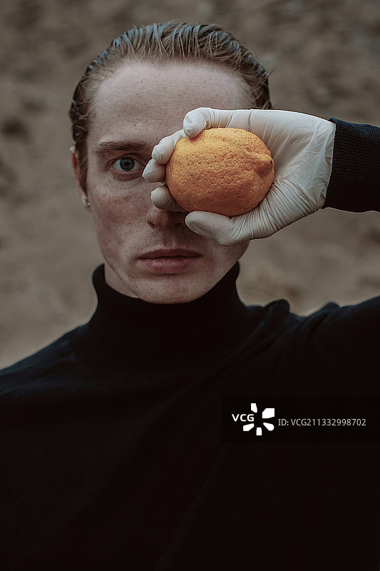 一个男人在他的眼睛前举着一个橙子的特写图片素材