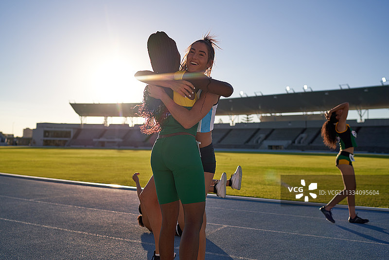 快乐的女性田径运动员拥抱在阳光的轨道上图片素材