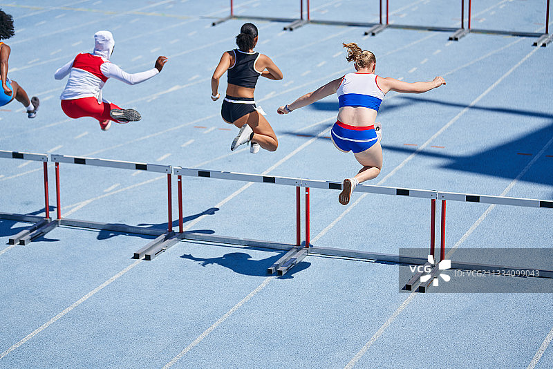 女子田径运动员在阳光跑道上跨栏图片素材