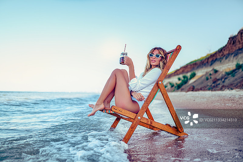 漂亮的女人在沙滩上休息，喝着苏打水图片素材