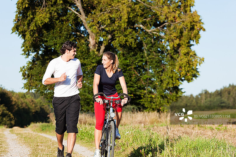 在晴朗的蓝天下，一对年轻的健身夫妇在户外做运动，慢跑和骑自行车图片素材