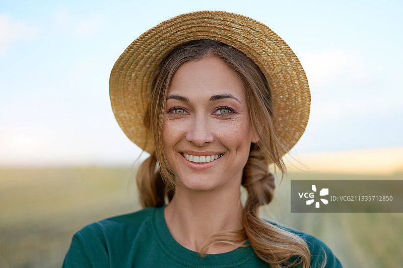 戴着帽子的微笑女人的肖像站在球场上，对着天空图片素材