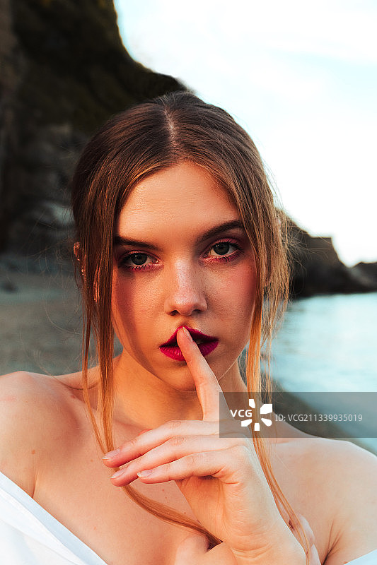 美丽的年轻女子的肖像与手指在海滩上的嘴唇，阿尔比索拉Superiore，萨沃纳，意大利图片素材