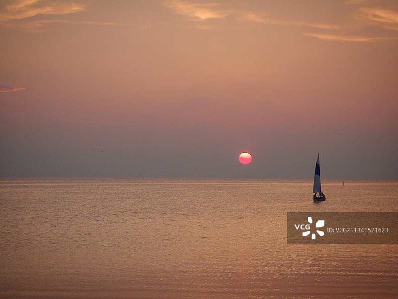日落时，天空映衬下海上帆船的剪影图片素材