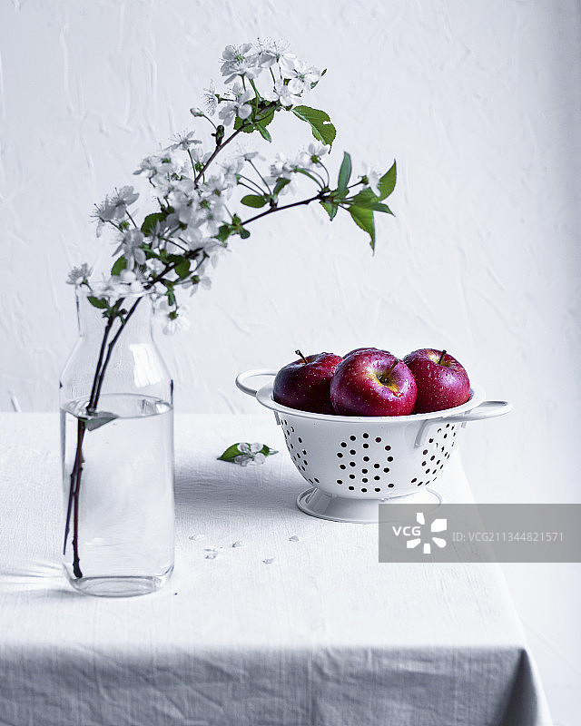桌子上的筛子里有红苹果，玻璃瓶里有苹果花枝图片素材