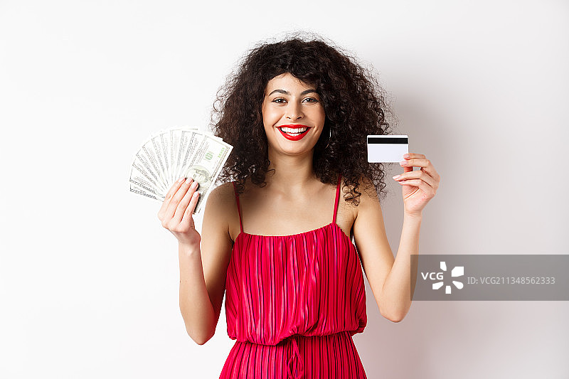 一名年轻女子手持信用卡，面带微笑，站在白色背景下图片素材