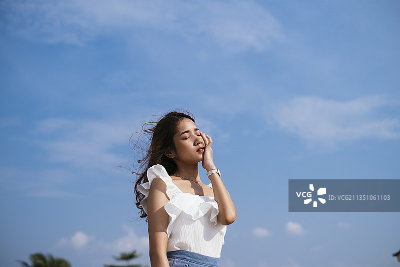 棕色皮肤性感美丽的亚洲泰国旅行者女人在刮风的日子在蓝色的天空背景。图片素材