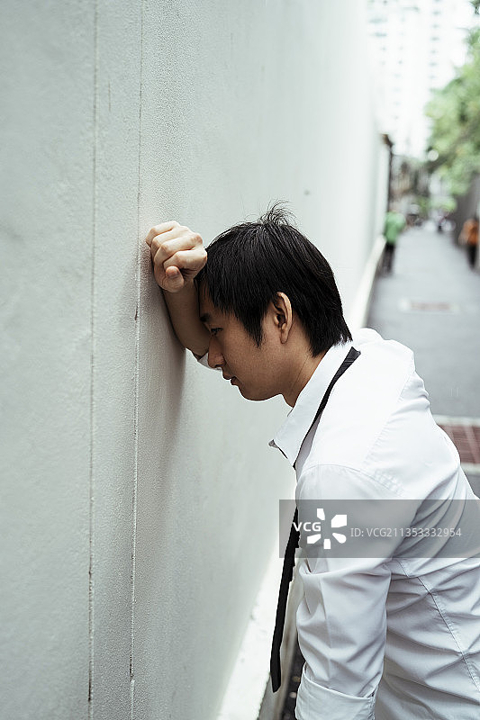 年轻的亚洲商人面对墙壁，把手放在墙上。紧张的亚洲商人与愤怒的摆姿势。图片素材