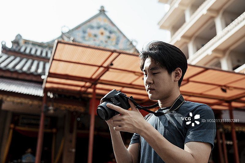 年轻英俊的亚洲摄影师男子持有相机旅行在中国寺庙。图片素材