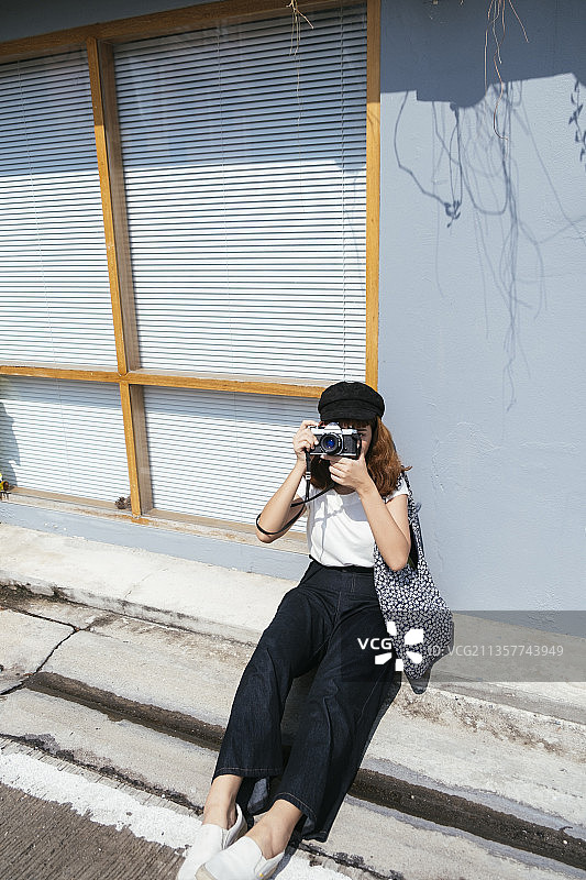 漂亮的年轻亚洲潮女用相机坐在街上。街头摄影师的女人。图片素材
