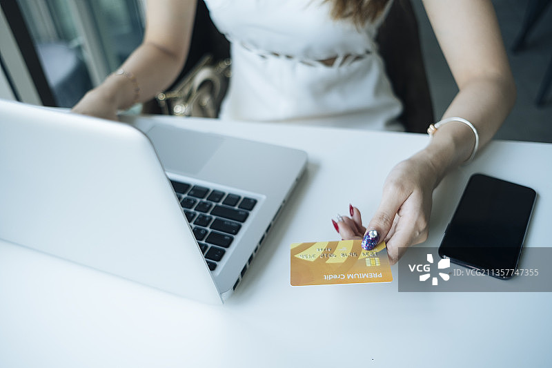 网上购物概念——漂亮的女人拿着信用卡，用它来做网上购物。用信用卡和笔记本电脑购物的女孩。图片素材