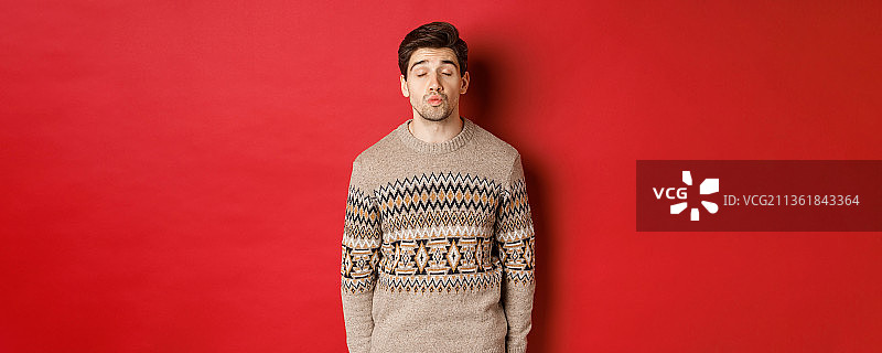 形象英俊的男人在圣诞节毛衣噘起嘴唇和闭上眼睛图片素材