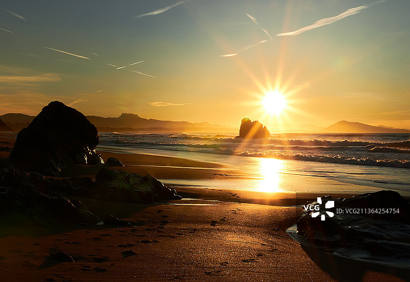 落日背景下的海滩上的岩石和山脉，西班牙图片素材