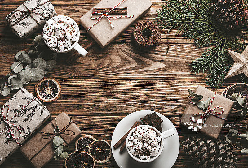 圣诞装饰背景与包装的礼物，冷杉树枝，棉花糖可可杯子木制的桌子。快乐的圣诞节包装礼盒顶部视图与复制空间模板图片素材