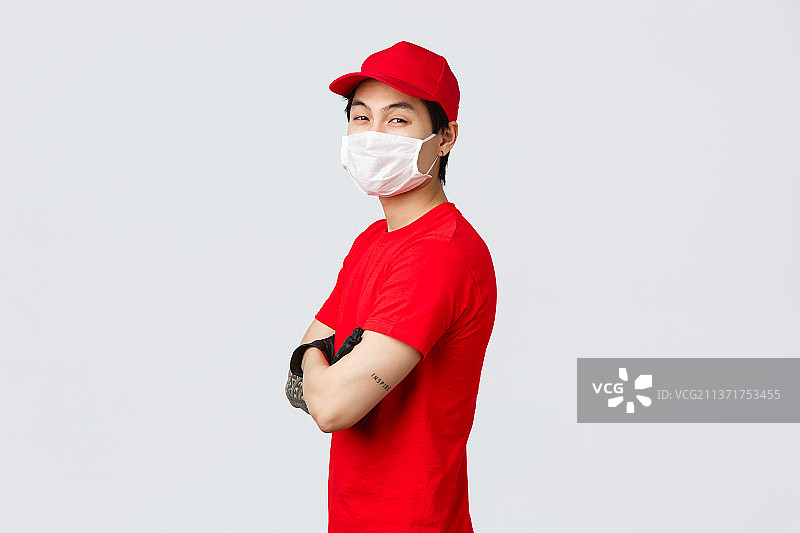 自信的亚洲送货员戴着红帽子，医用口罩和手套图片素材