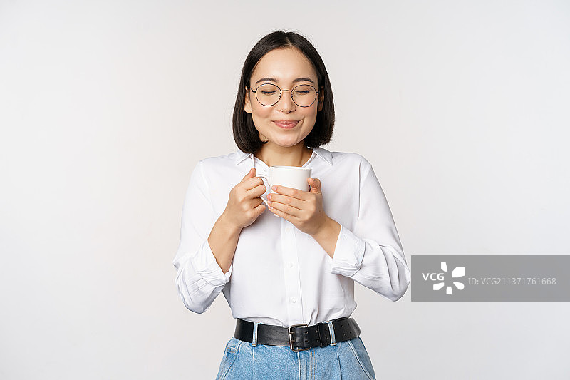 微笑的韩国女人，闻闻杯子里的咖啡，享受图片素材