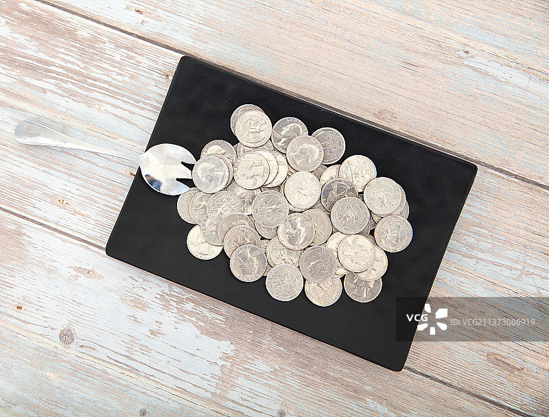 俯视桌子上盛满美元硬币的盘子和一把勺子图片素材