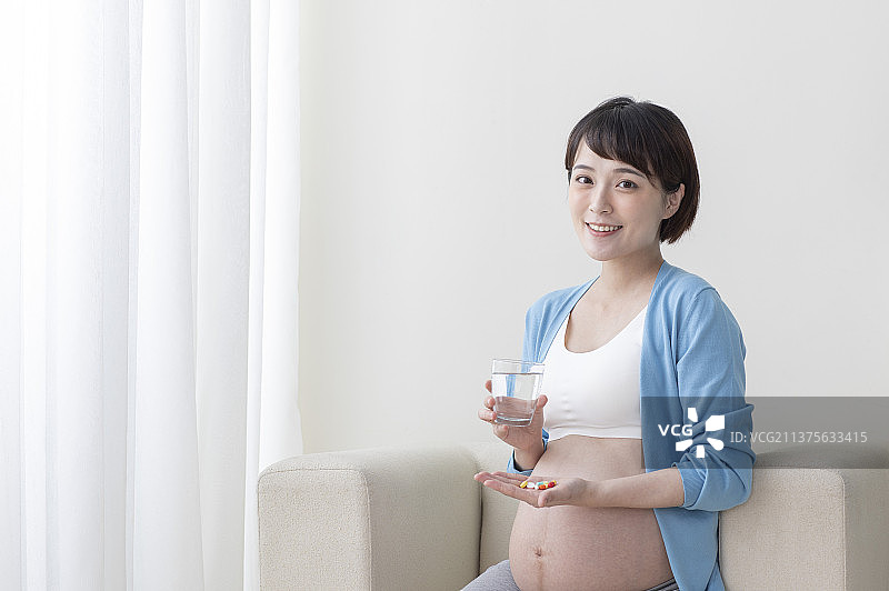 孕妇拿着杯子坐在沙发上吃药图片素材