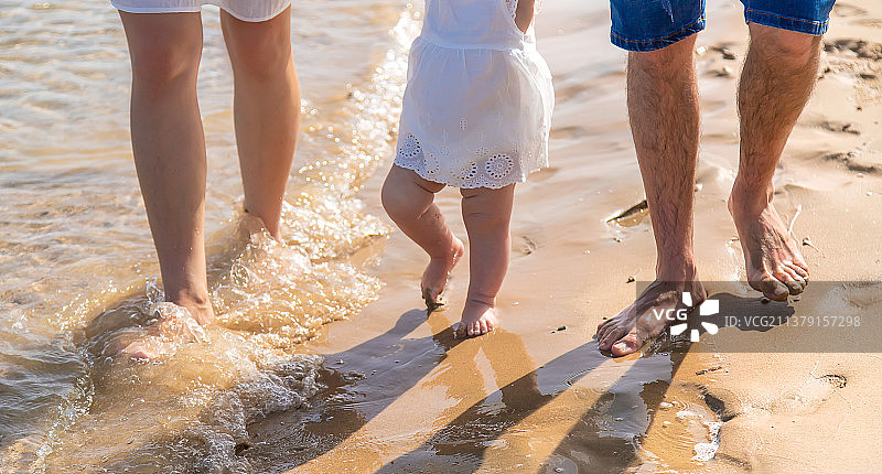 宝宝和爸爸妈妈在海滩上散步选择性聚焦图片素材