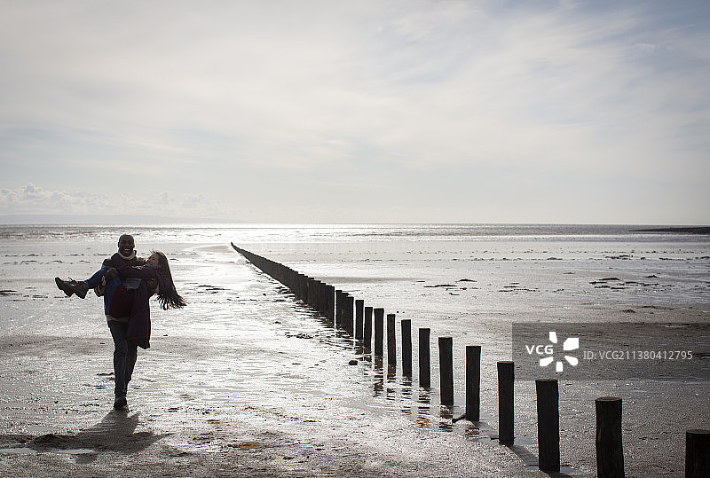 男友背着女友在阳光明媚潮湿的冬季海滩上图片素材