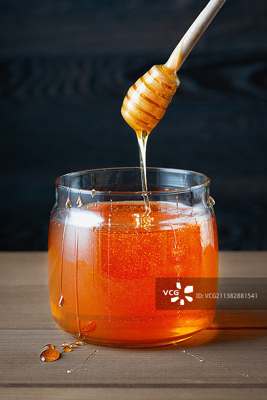 蜂蜜在罐子与蜂蜜勺在质朴的木制背景图片素材