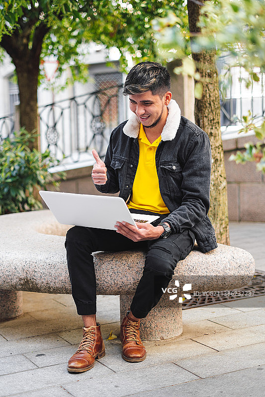 西班牙，萨拉曼卡，一个拉丁男子坐在公园的石凳上，手里拿着一台笔记本电脑图片素材