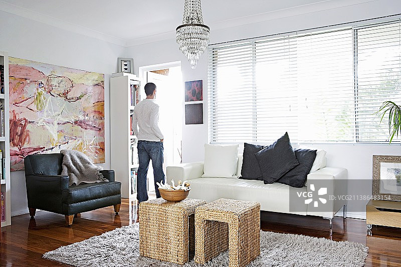 客厅的休息区配有复古皮革扶手椅和编织边桌;站在窗前的年轻人图片素材
