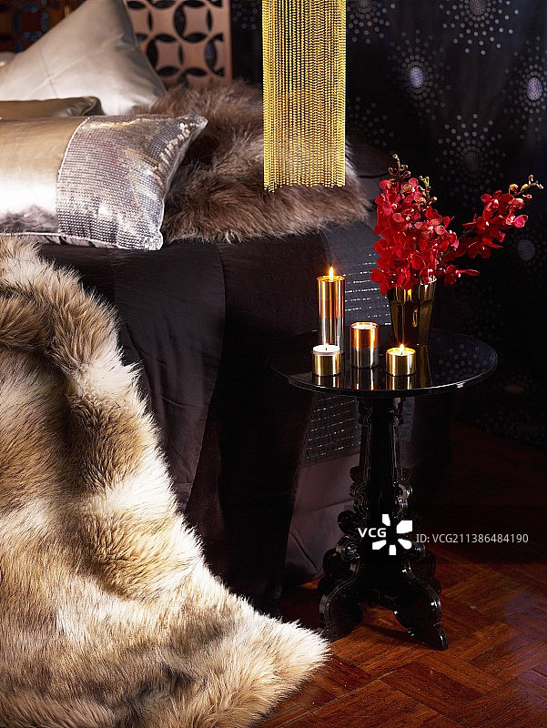 毛皮毛毯，黑色的边桌，点燃的金色蜡烛和红色兰花在迷人的卧室图片素材