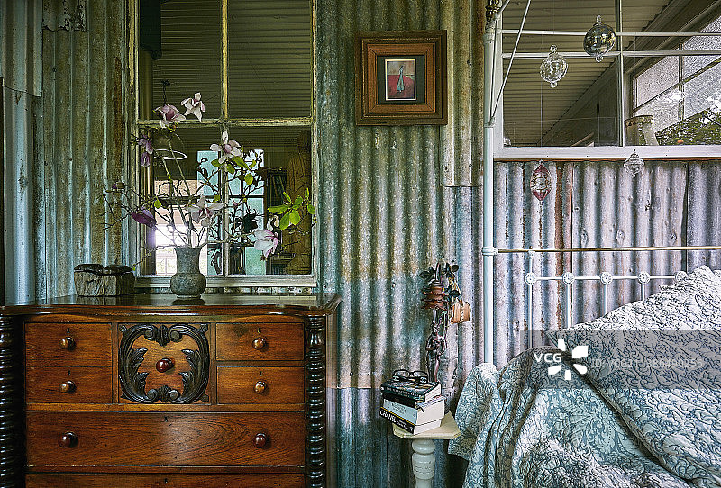 古董抽屉柜紧挨着金属床，有波纹铁墙的复古卧室图片素材