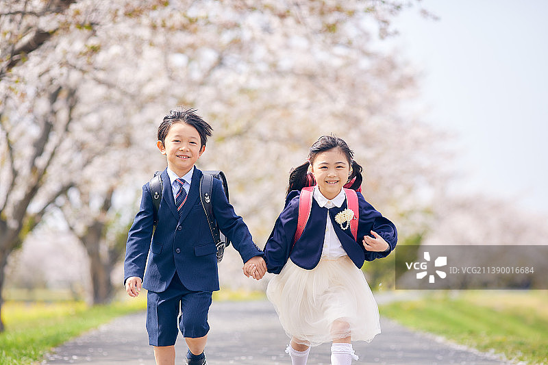 日本小学生牵手在樱花下奔跑图片素材