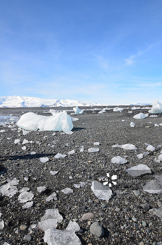 蓝色的天空，黑色的沙滩上有大块的冰川图片素材