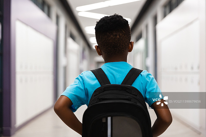 非洲裔美国小学生背双肩包站在学校走廊的背影图片素材