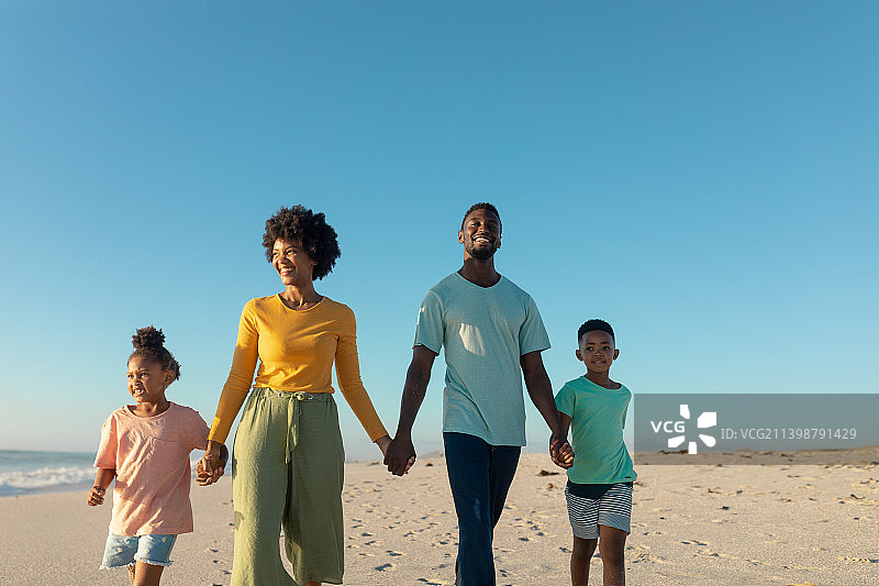快乐的非洲裔美国家庭散步，而牵手在海滩上对蓝天的拷贝空间图片素材