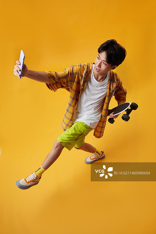 手拿滑板玩手机的年轻男孩图片素材